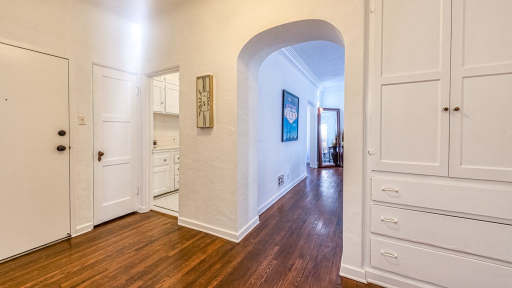 a living room with an archway and a hallway with white cabinets and wood floors