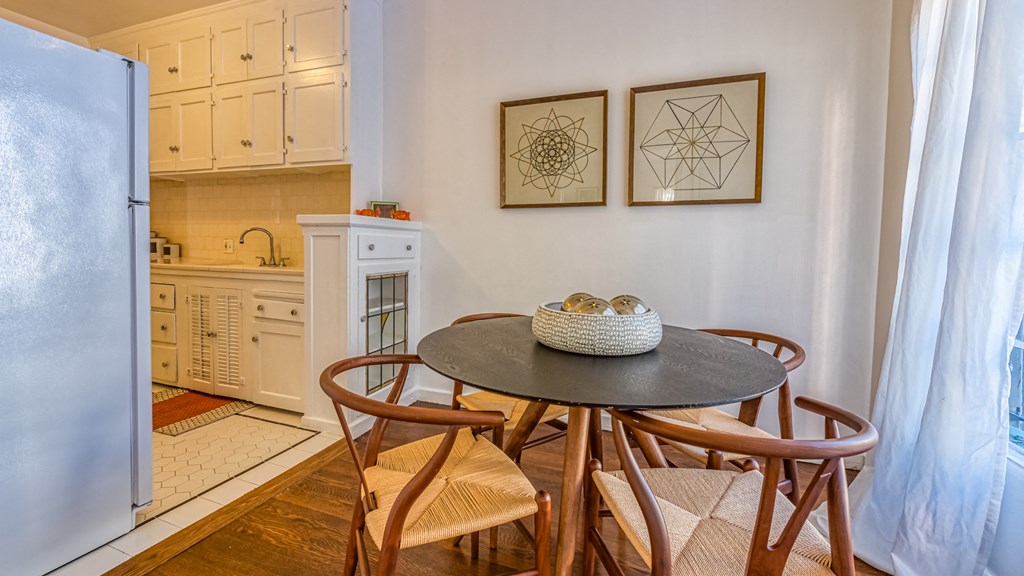a dining area with a table and chairs and a kitchen with a refrigerator