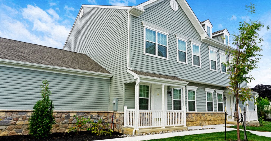 the front of a gray house with a stone wall