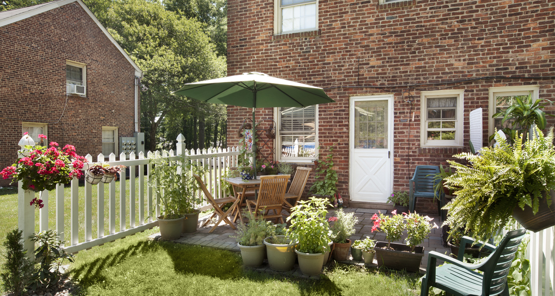 a small yard with a white fence and a patio with chairs and an umbrella