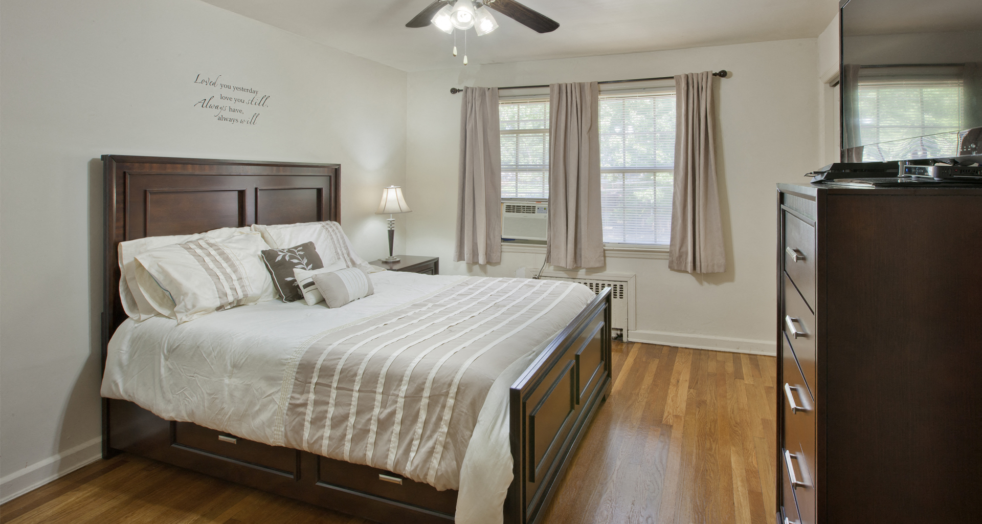 a bedroom with a bed and a dresser and two windows