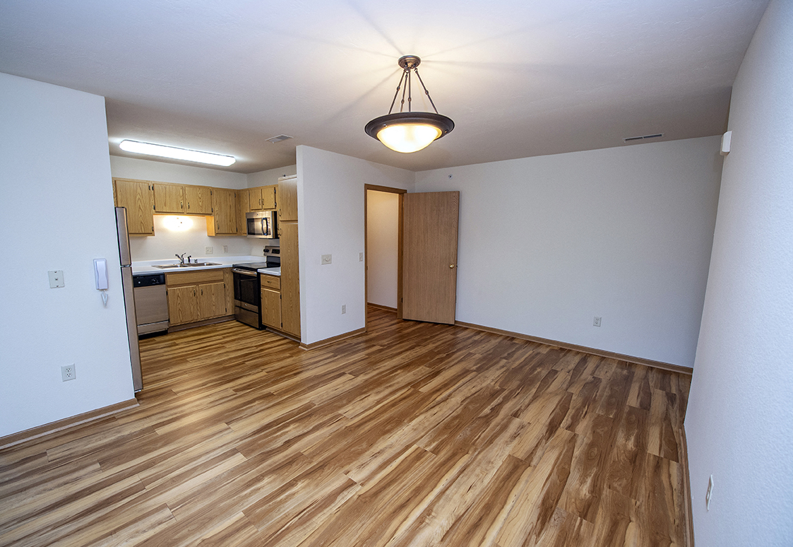 an empty living room with wood flooring and a kitchen