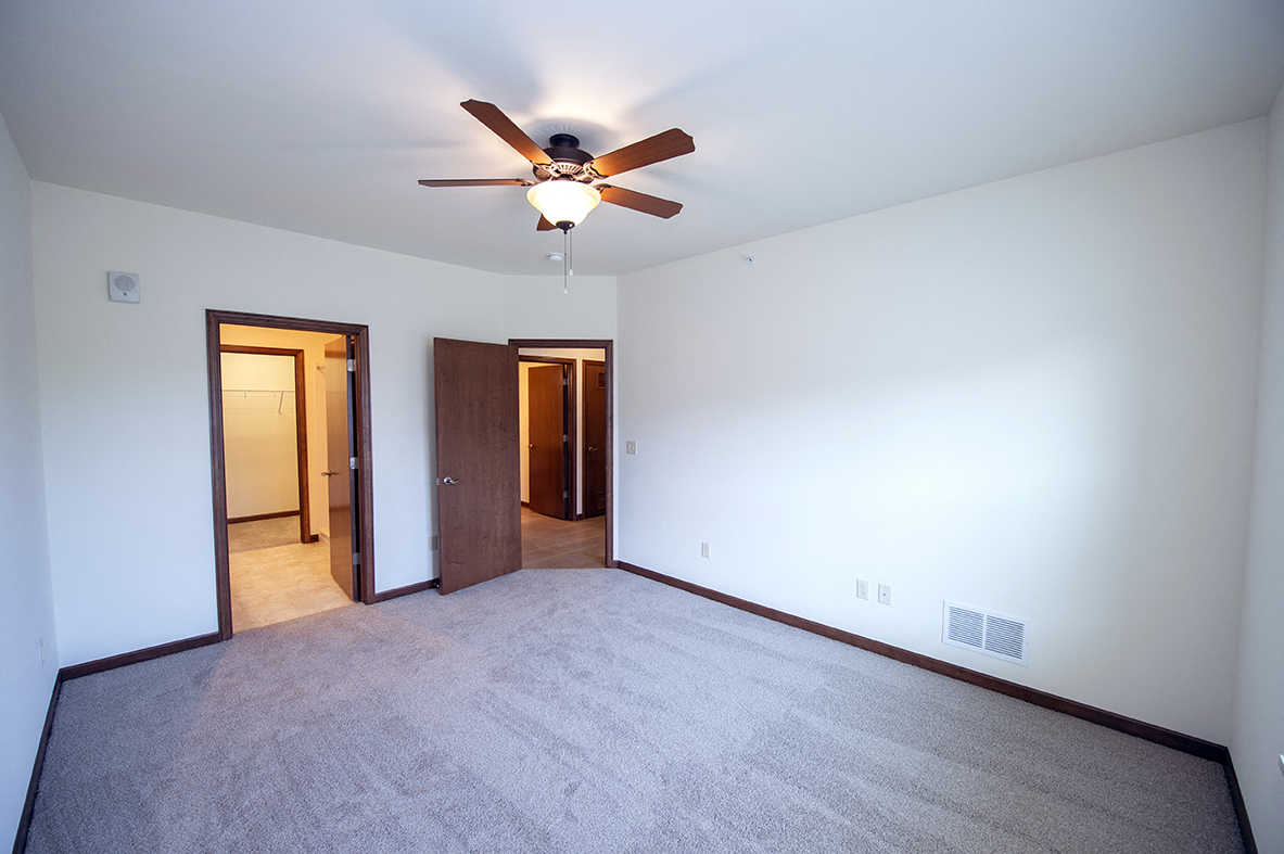 an empty living room with a ceiling fan and a white wall