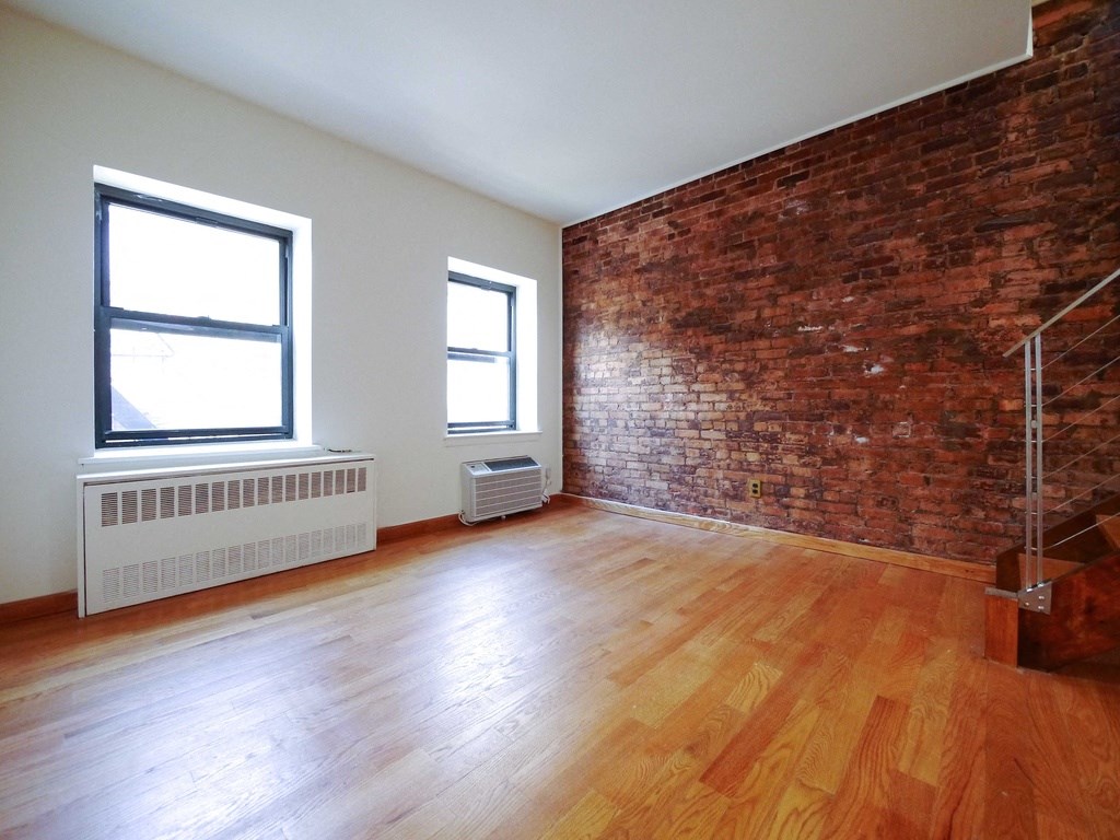 an empty living room with a brick wall and wooden floors
