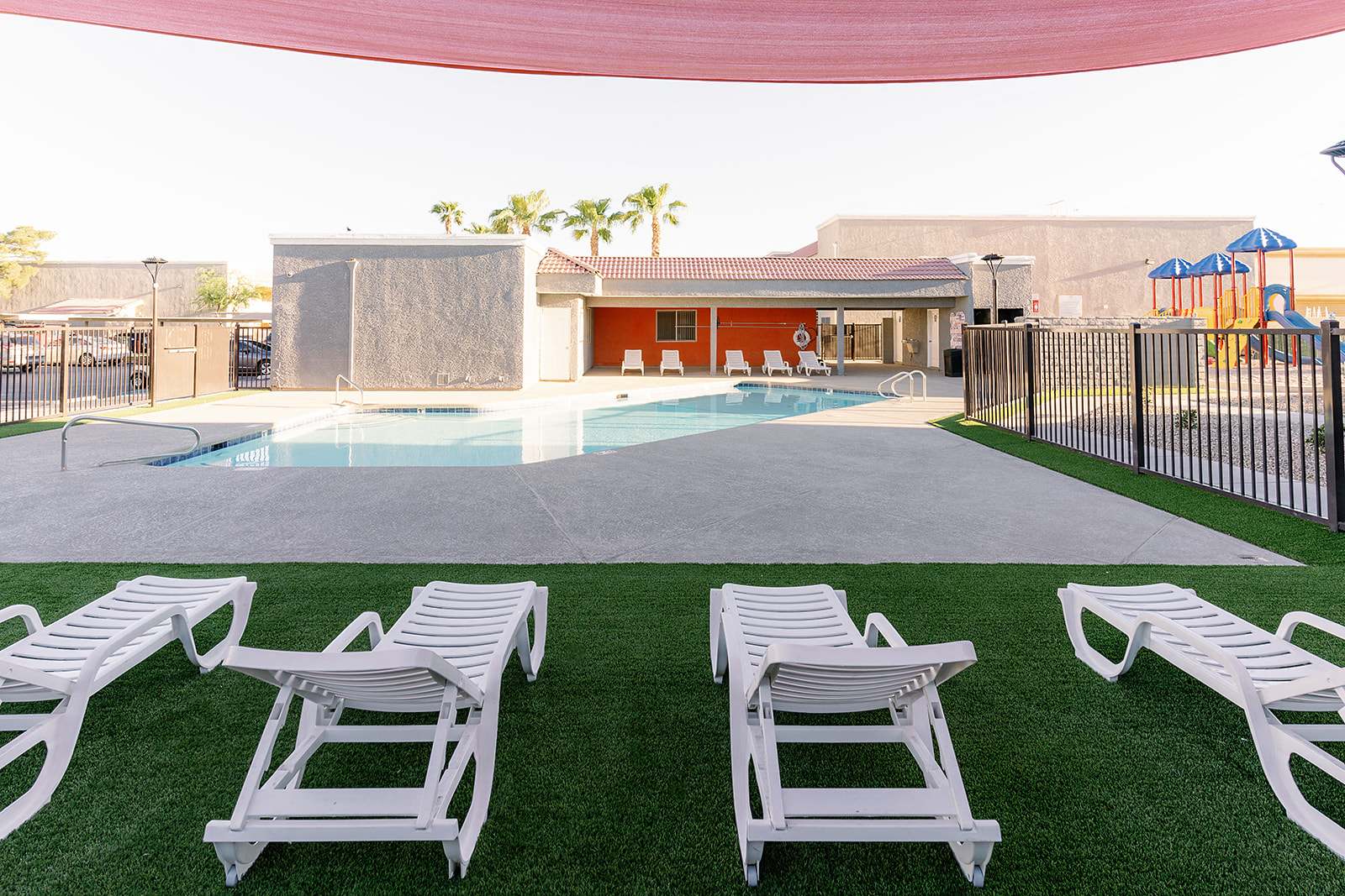a pool with white lounge chairs in front of a building