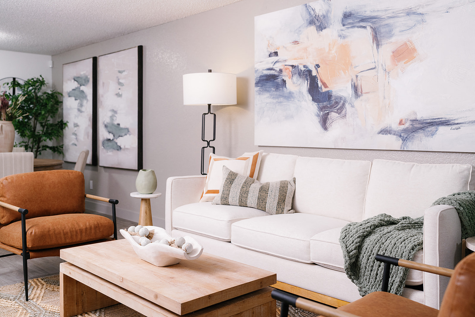 A living room with a white couch, a wooden coffee table, and a large abstract painting on the wall.