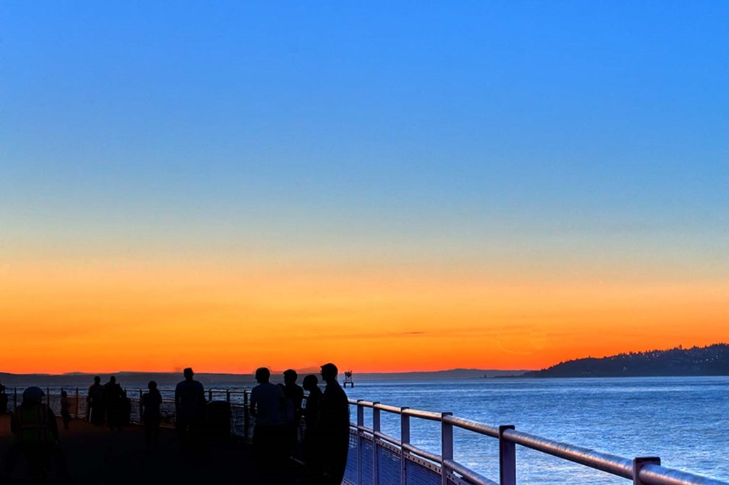people watching the sunset from a pier over the ocean