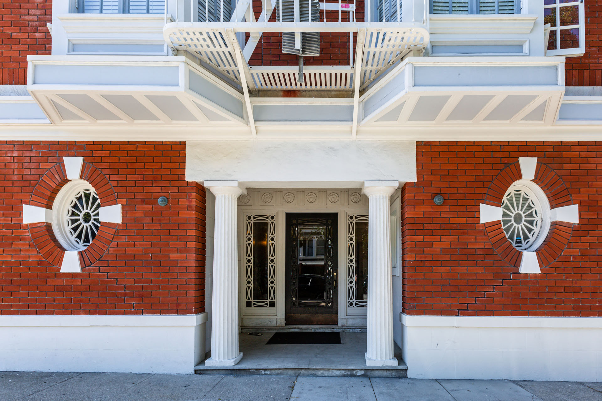 A red brick building with a white balcony and two white columns on either side of the door.