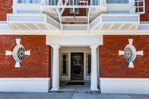 A red brick building with a white balcony and two white columns on either side of the door.