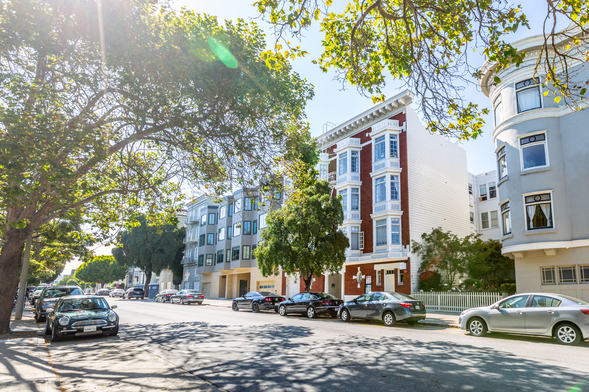 Cars parked on a street with trees and buildings on either side.