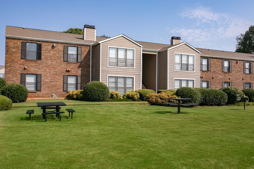 a large brick apartment building with a green lawn and picnic table