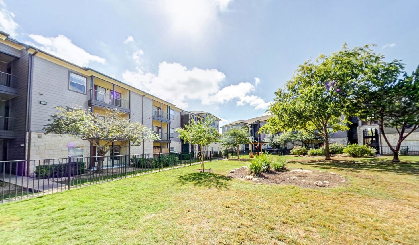 Fenced in dog park with large green space and shade trees