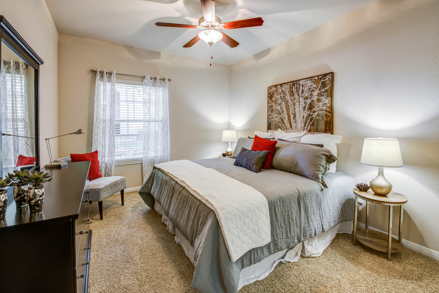 Apartments In Austin, TX - Spacious Bedroom With Plush Carpet Flooring, Ceiling Fan, Large Window, And Modern Décor.