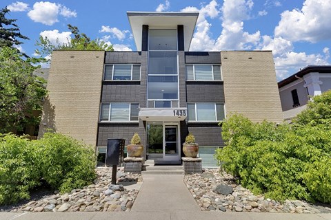 the front of a condo building with a sidewalk and plants
