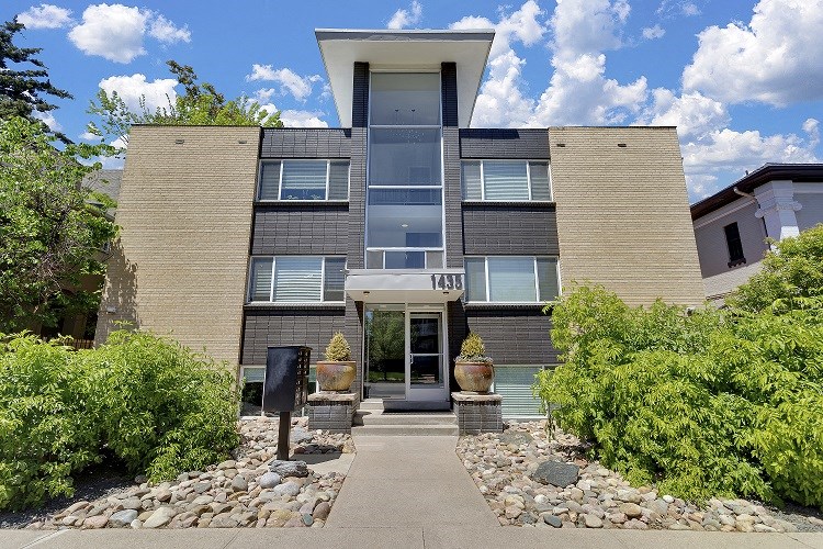 the front of a condo building with a sidewalk and plants