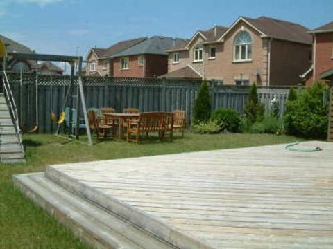 A wooden deck with a table and chairs is in the foreground of a residential area.