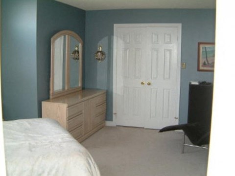 A bedroom with a bed, dresser, mirror and chair.