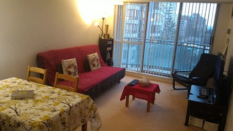 A bedroom with a bed, a couch, a chair, a small table, and a television.