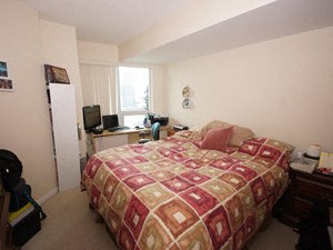 A bedroom with a bed, desk, chair, and window.