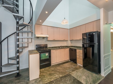 A kitchen with a black refrigerator and a spiral staircase.
