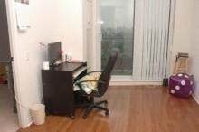 A black computer desk with a monitor, keyboard, and mouse sits in a room with a black office chair.