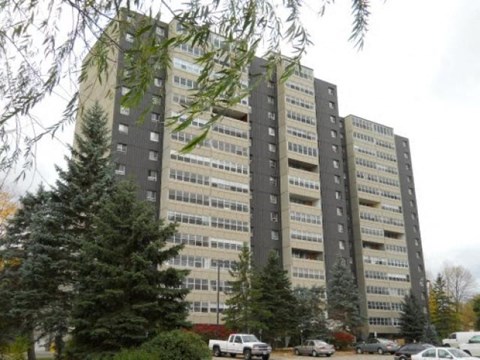 A tall building with many windows and cars parked in front.