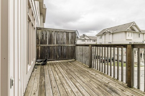 A wooden deck with a bench and a building in the background.