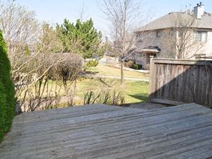 A wooden deck overlooks a backyard with a house and trees.