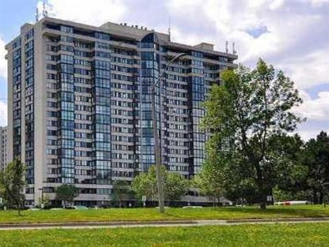 A large, modern building with many windows is surrounded by trees and grass.