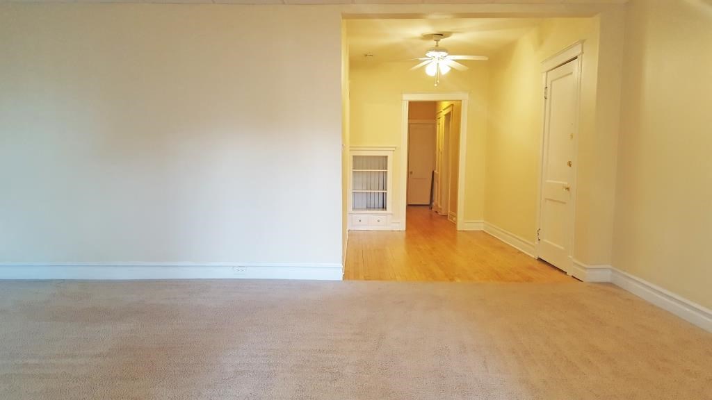an empty living room with a carpet and a ceiling fan