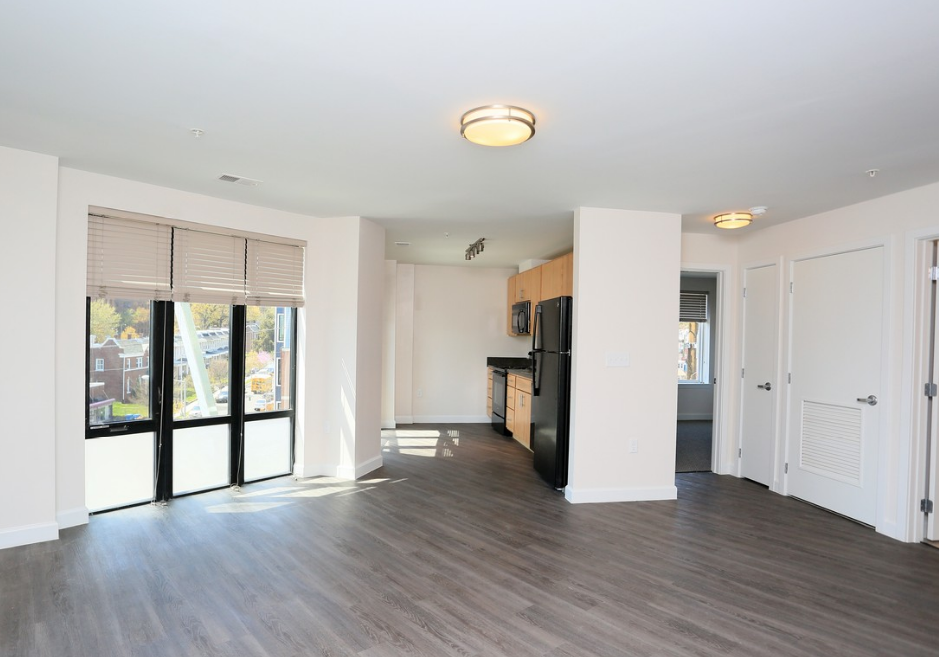 the living room and kitchen of an apartment with a wood floor and a large window