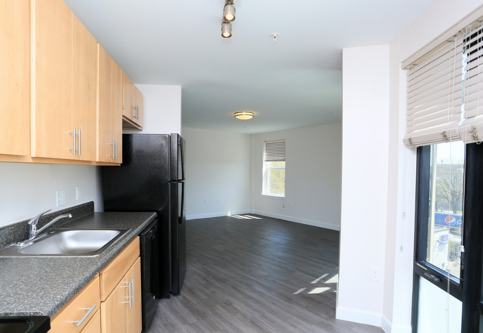 a kitchen and living room with wood flooring and a black refrigerator