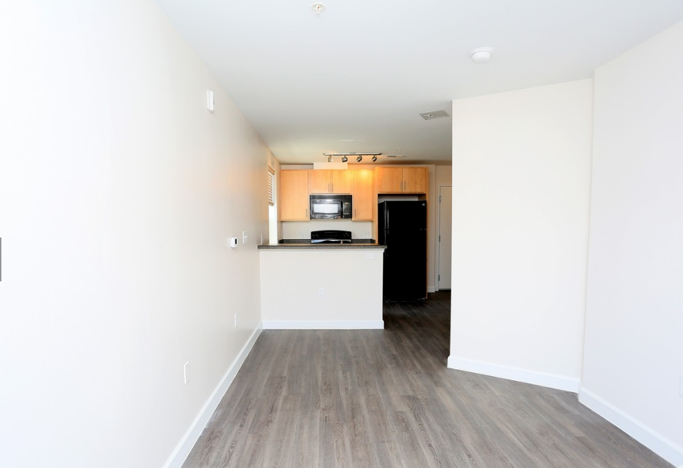 an empty living room and kitchen with white walls and wood floors