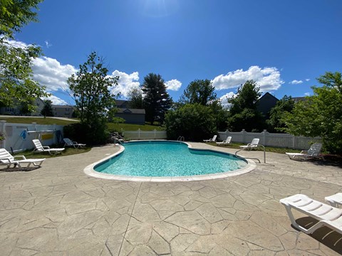 A pool surrounded by a stone patio and lawn chairs.