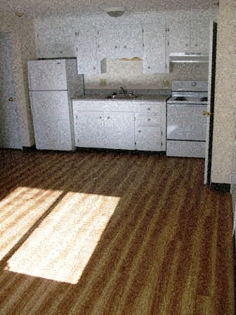 an empty kitchen with white appliances and a wooden floor