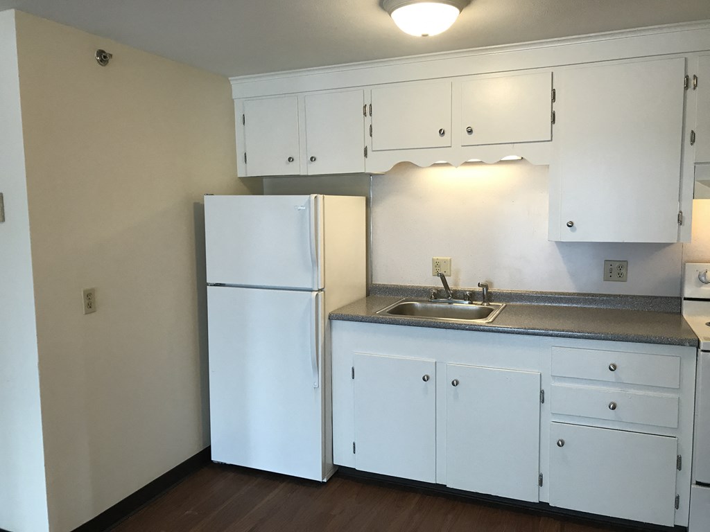 an empty kitchen with white cabinets and a white refrigerator