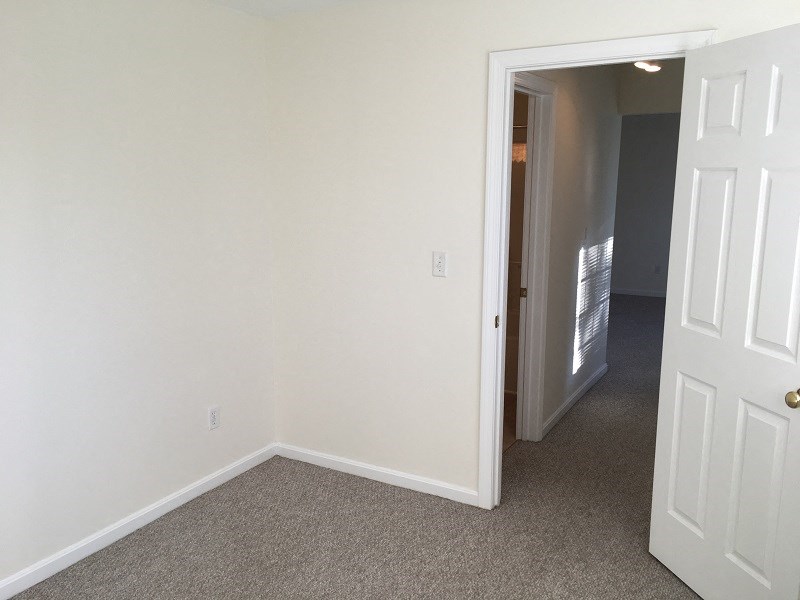 an empty bedroom with white walls and a door to a hallway