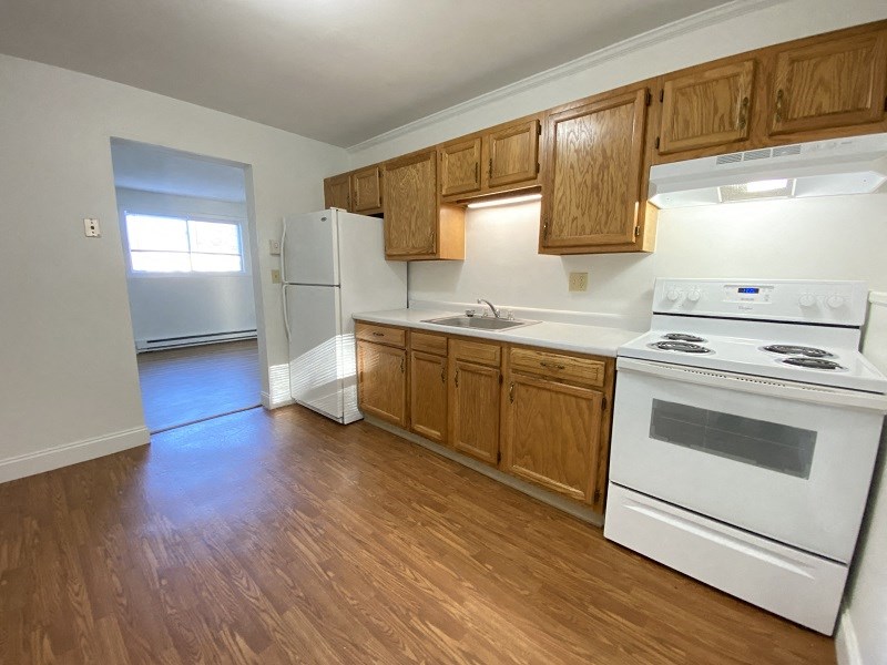 an empty kitchen with wood flooring and white appliances
