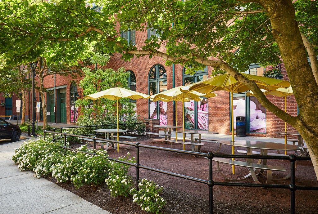 a courtyard with tables and umbrellas in front of a brick building