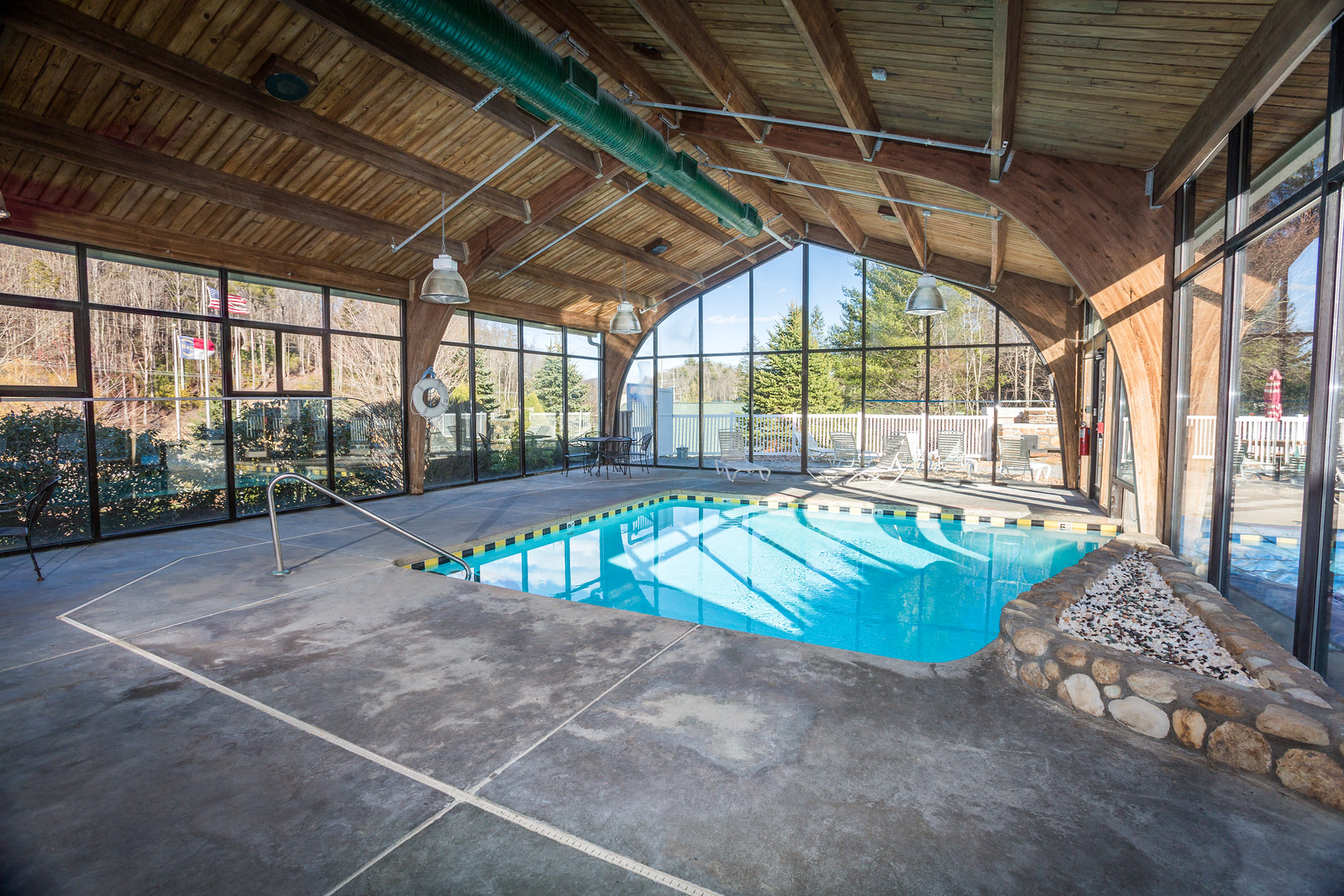 a swimming pool in a building with glass walls and a wood ceiling