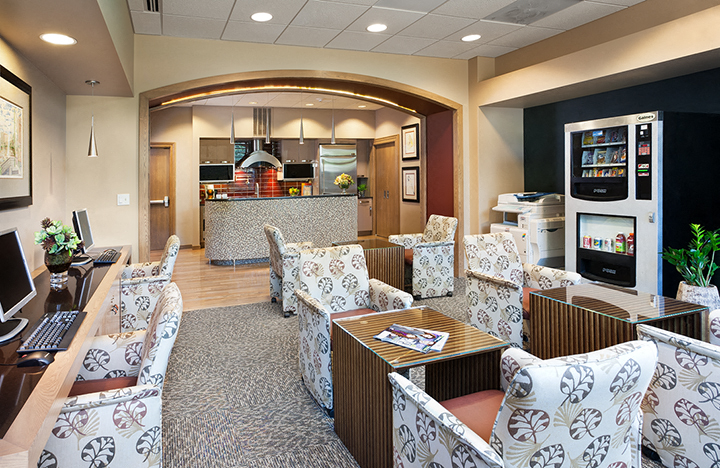 a lobby with chairs and a table with a kitchen in the background