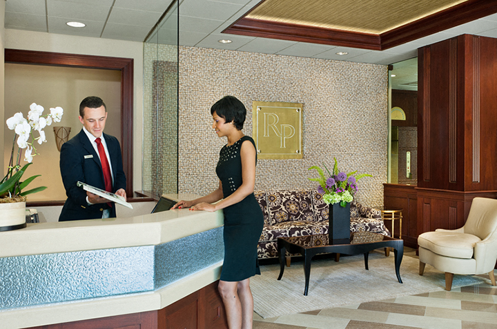a man and woman standing at the front desk of a hotel lobby