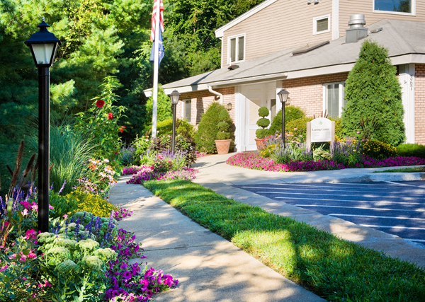 a sidewalk in front of a house with flowers and a flag