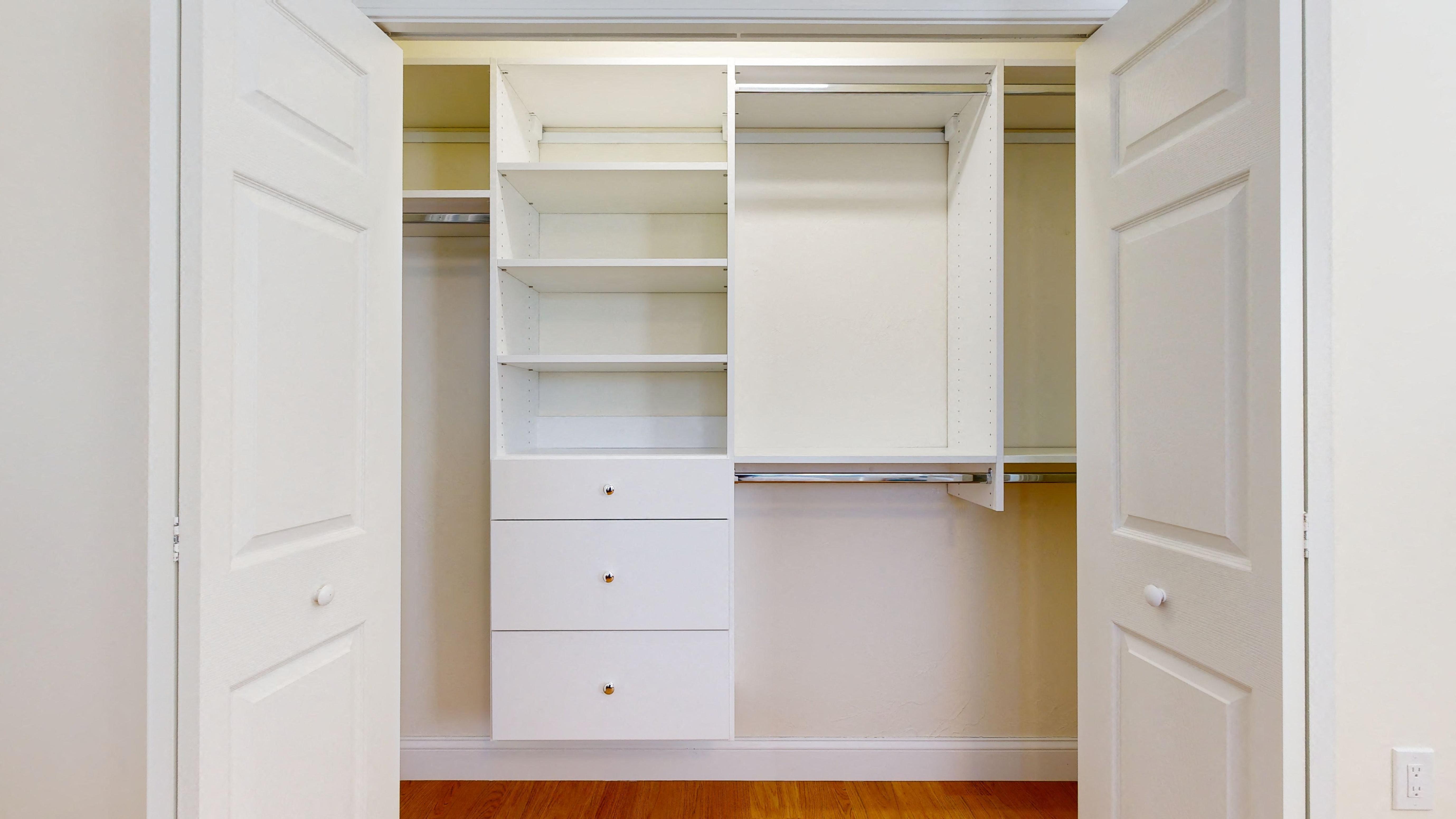 a walk in closet with white shelves and drawers and