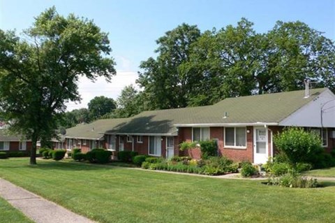 A row of houses with green lawns and trees in the background.