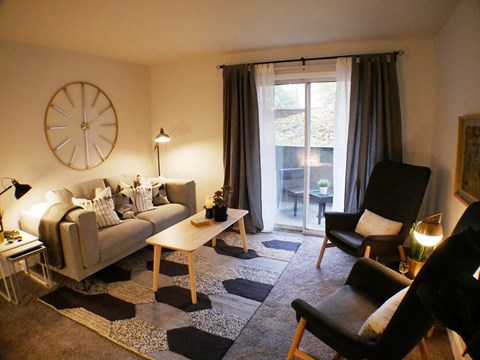A living room with a couch, chairs, and a clock on the wall.