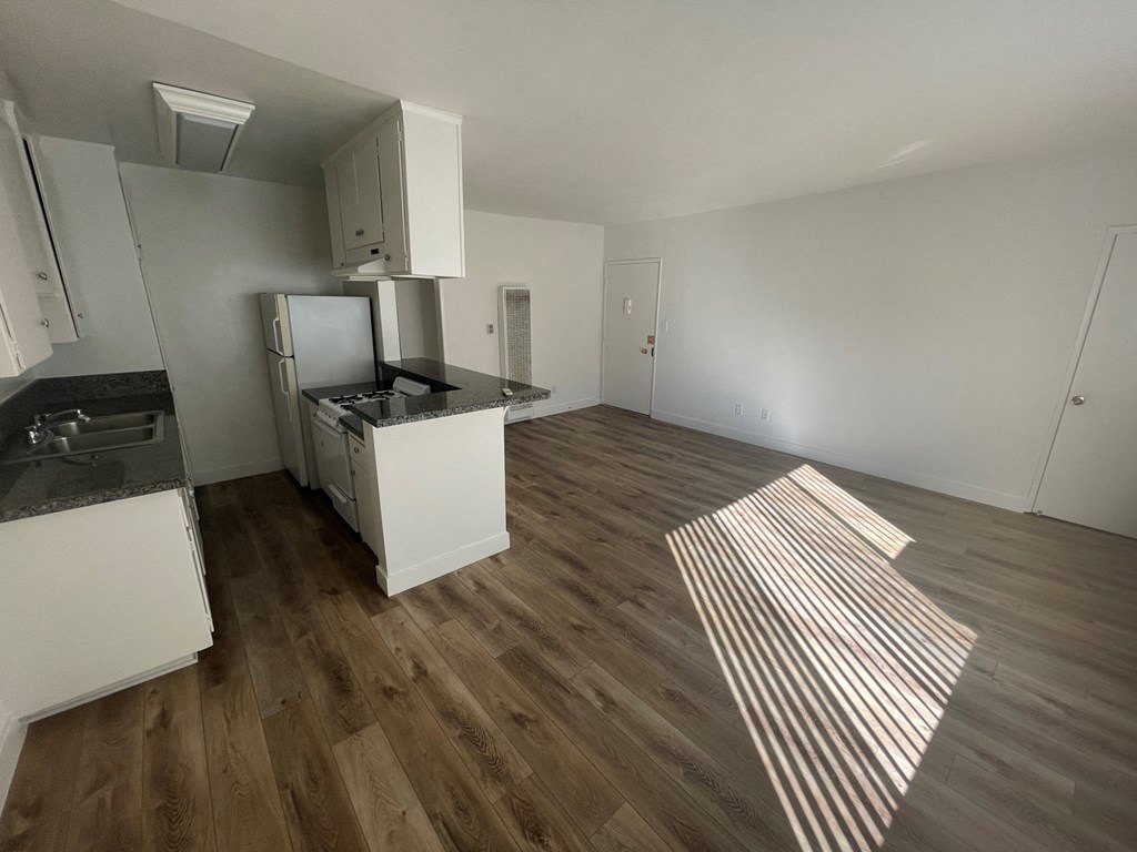 an empty kitchen and living room with wood floors and white cabinets