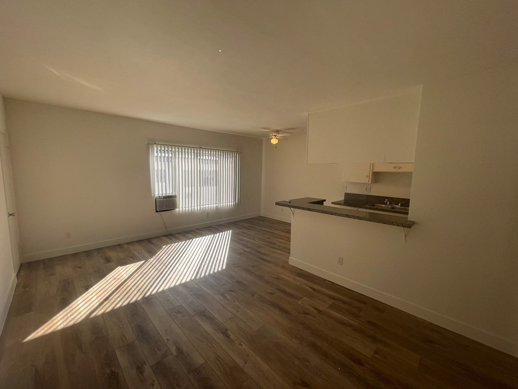 an empty living room with a kitchen and a window