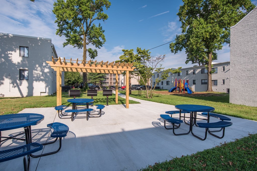 a patio with picnic tables and a wooden pavilion with a playground in the background