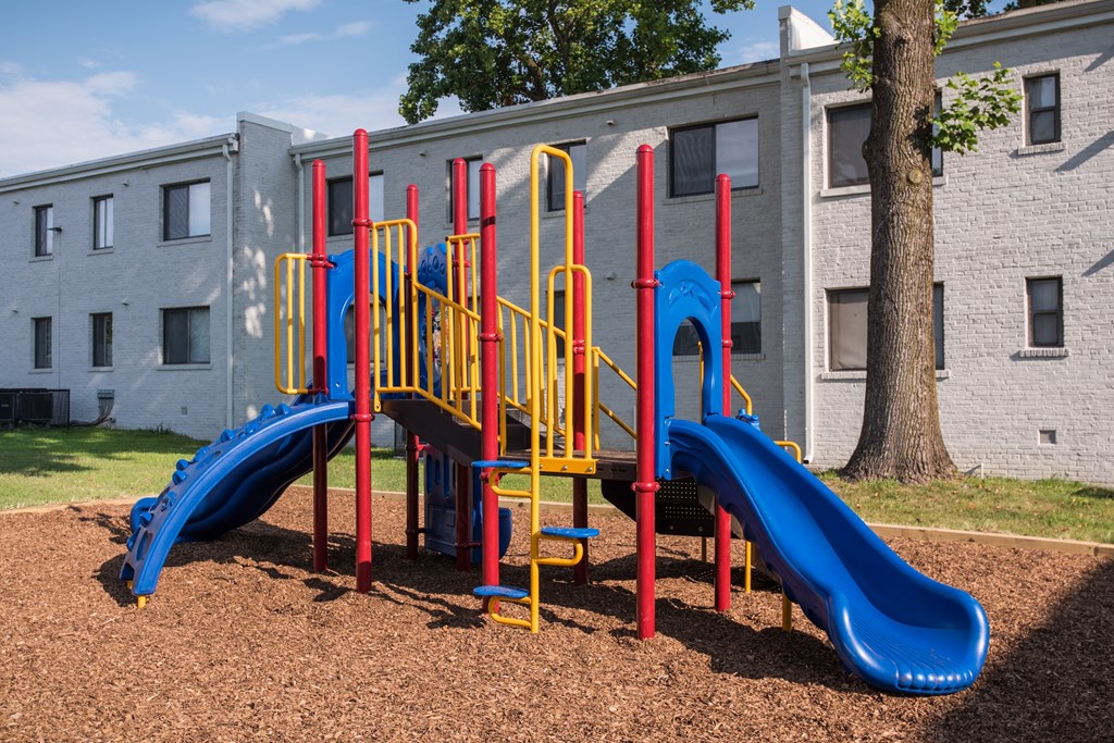 a playground with two slides and a tree in front of a building